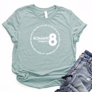 May include: A light blue t-shirt with a white circle graphic that says "Romans 8:Twenty" and "To His Purpose All Things Work Together For Good To Them That Love God, To Them Who Are The Called According To His Purpose".