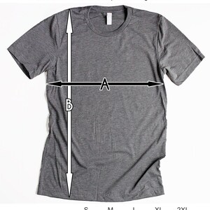 Op de afbeelding: Een grijs T-shirt met een maattabel die de breedte van het lichaam en de lengte van het lichaam in inches aangeeft voor de maten S, M, L, XL en 2XL.