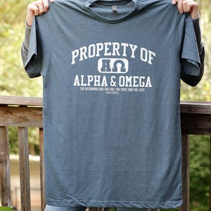 Pu&ograve; includere: Una maglietta blu con testo bianco che recita "PROPERTY OF &Pi;&Omega; ALPHA & OMEGA THE BEGINNING AND THE END, THE FIRST AND THE LAST. REVELATION 22"