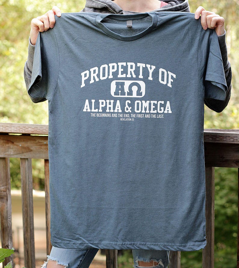 Pu&ograve; includere: Una maglietta blu con testo bianco che recita "PROPERTY OF &Pi;&Omega; ALPHA & OMEGA THE BEGINNING AND THE END, THE FIRST AND THE LAST. REVELATION 22"