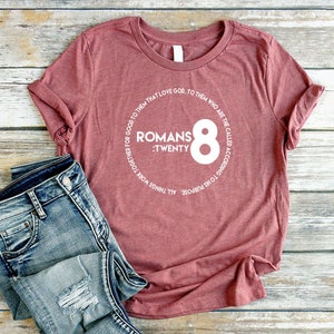 May include: A maroon t-shirt with a white circle graphic featuring the text "Romans :Twenty 8" and a white circle around the text.