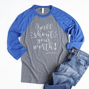 May include: A gray and royal blue baseball tee shirt with the text "I will shout your worth! Psalm 139:13" printed in white on the front.