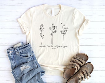 May include: A beige t-shirt with a black line drawing of three wildflowers and the text "consider how the wildflowers grow" and "LUKE 12:27".