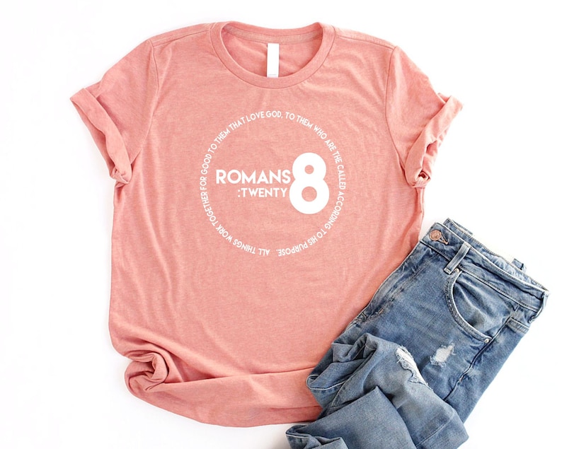 May include: A pink t-shirt with a white circle graphic that says "Romans 8:Twenty" and "All things work together for good to them that love God. To them who are the called according to His purpose."