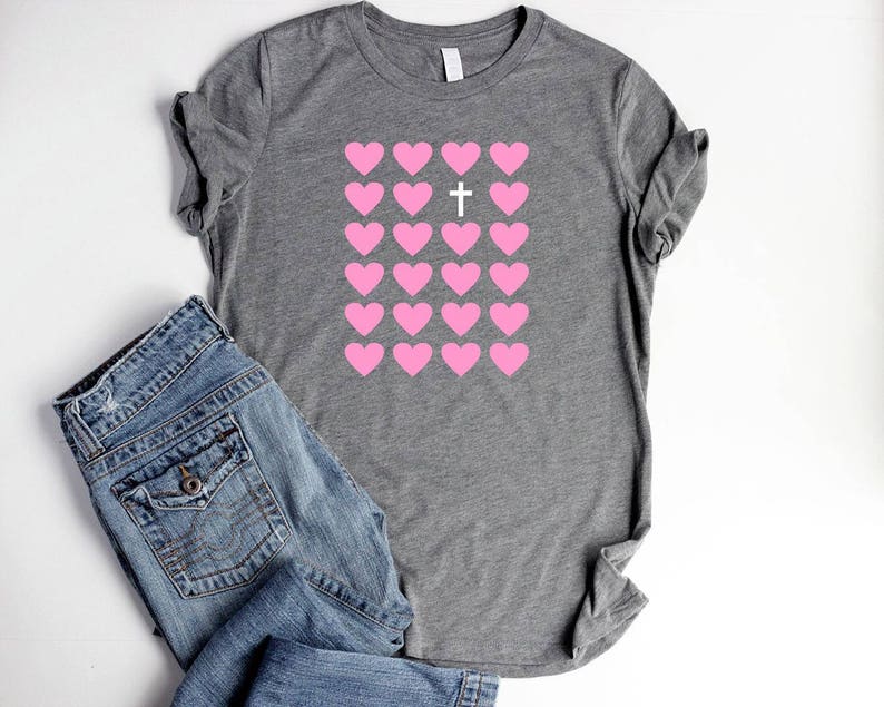 May include: A gray t-shirt with a pattern of pink hearts and a white cross in the center of the hearts.