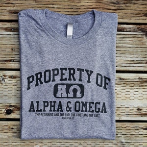 Pu&ograve; includere: Maglietta grigia con testo nero che recita "PROPERTY OF &Alpha;&Omega; ALPHA & OMEGA THE BEGINNING AND THE END, THE FIRST AND THE LAST REVELATION 1:8"