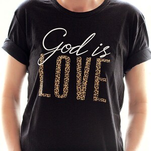 May include: Black t-shirt with white text that says "God is Love" with a leopard print design behind the word "Love".