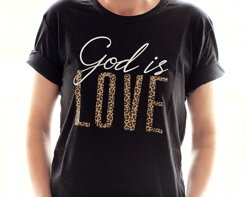 May include: Black t-shirt with white text that says "God is Love" with a leopard print design behind the word "Love".
