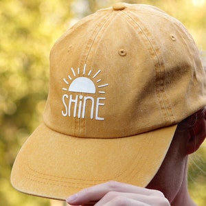 May include: A yellow baseball cap with a white sun and the word "SHINE" on the front.