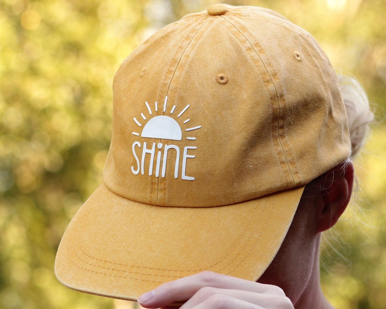 May include: A yellow baseball cap with a white sun and the word "SHINE" on the front.