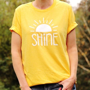 May include: A yellow t-shirt with a white sun and the word "SHINE" printed on the front.
