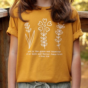 May include: Mustard yellow t-shirt with a white graphic of three stylized flowers and the text "grow in the grace and knowledge of our Lord and Savior Jesus Christ 2 Peter 3:18"