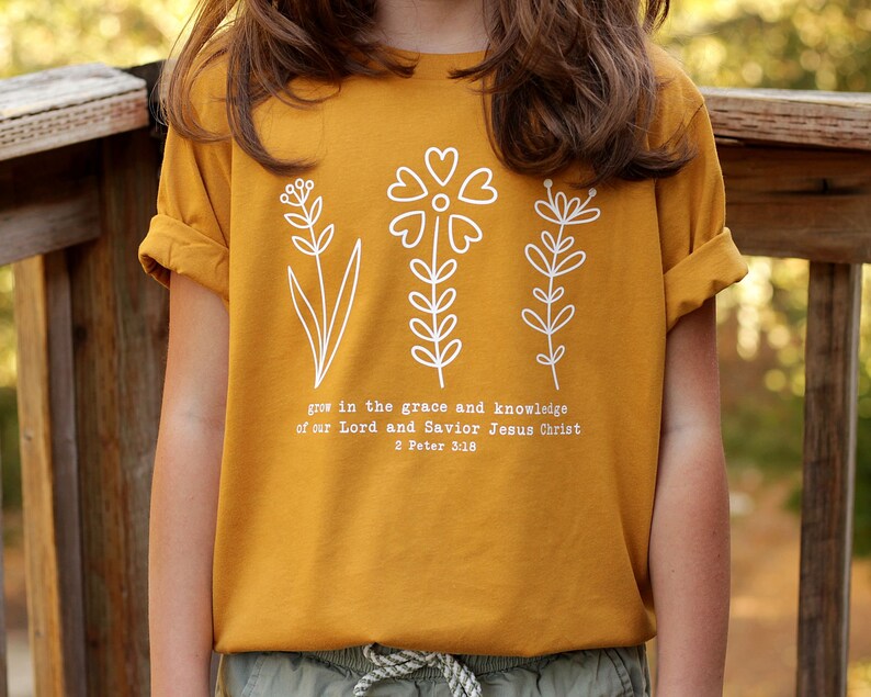 May include: Mustard yellow t-shirt with a white graphic of three stylized flowers and the text "grow in the grace and knowledge of our Lord and Savior Jesus Christ 2 Peter 3:18"