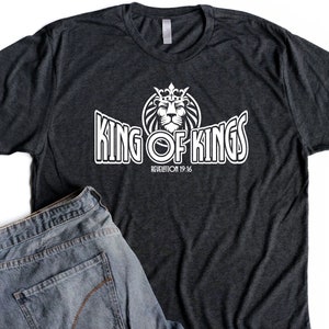 May include: A dark grey t-shirt with a white graphic of a lion wearing a crown and the text "King of Kings" with the scripture reference "Revelation 19:16".