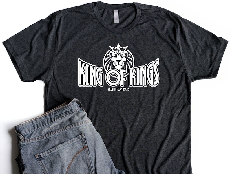 May include: A dark grey t-shirt with a white graphic of a lion wearing a crown and the text "King of Kings" with the scripture reference "Revelation 19:16".