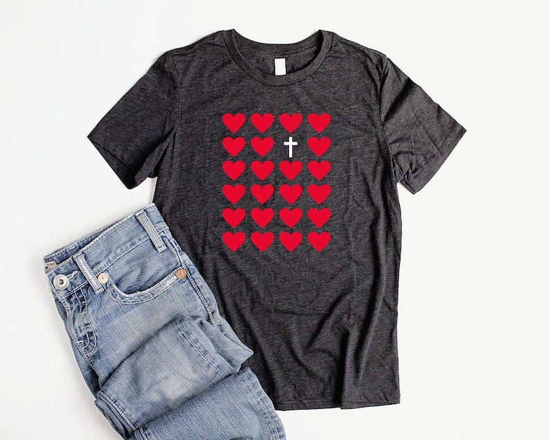 May include: A dark grey t-shirt with a pattern of red hearts and a white cross in the center. The hearts are arranged in a grid pattern.