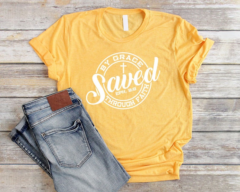 May include: A yellow t-shirt with a white circle graphic that says "Saved by Grace through Faith" with a cross and the scripture reference "Eph. 2:8".