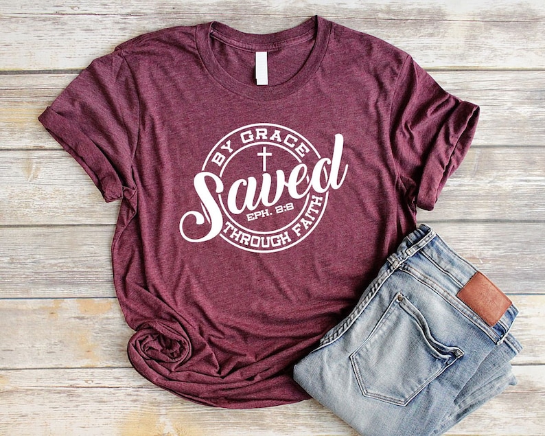 May include: A maroon t-shirt with a white circle graphic that says "Saved by Grace through Faith" with a cross and the scripture reference "Eph. 2:8".