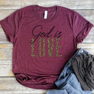 May include: Burgundy t-shirt with the text "God is Love" in black script. The word "Love" is printed in a leopard print pattern.