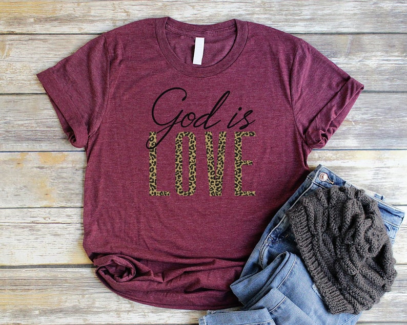 May include: Burgundy t-shirt with the text "God is Love" in black script. The word "Love" is printed in a leopard print pattern.