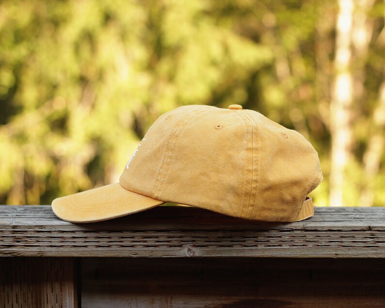 May include: A yellow baseball cap with a slightly distressed look. The cap is sitting on a wooden surface.