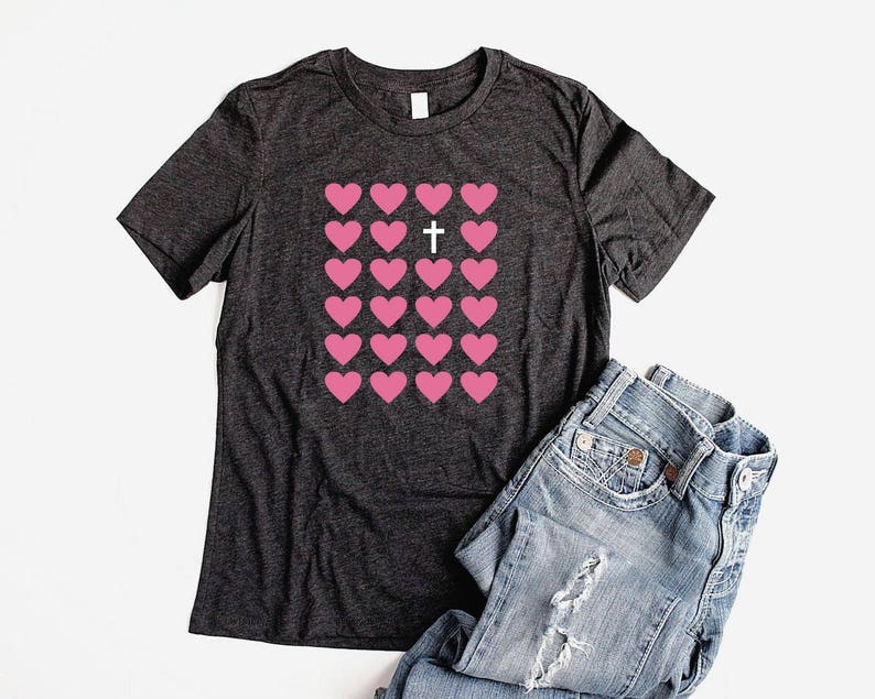 May include: A dark gray t-shirt with a pink heart design and a white cross in the center of the hearts.