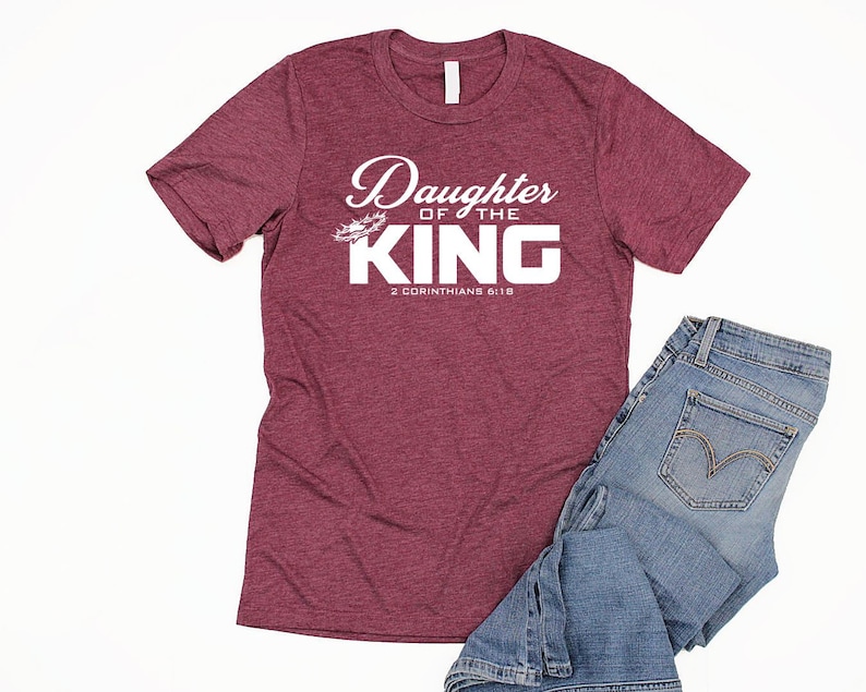 Op de afbeelding: Bordeauxkleurig heather t-shirt met witte tekst die "Daughter of the King" en "2 Corinthians 6:18" zegt.