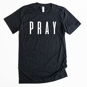 May include: A dark gray t-shirt with the word "PRAY" printed in white on the front.