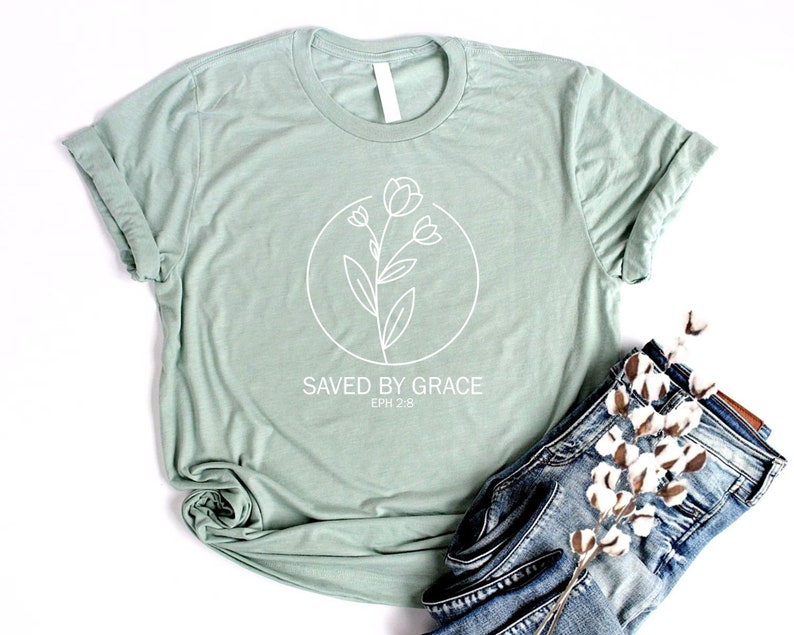 K&ouml;nnte beinhalten: Ein hellgr&uuml;nes T-Shirt mit einem wei&szlig;en Blumenmuster und dem Text "SAVED BY GRACE EPH 2:8".