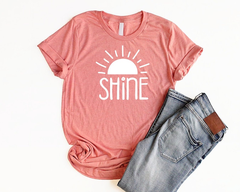 May include: A coral pink t-shirt with a white graphic of a sun with the word "shine" underneath.