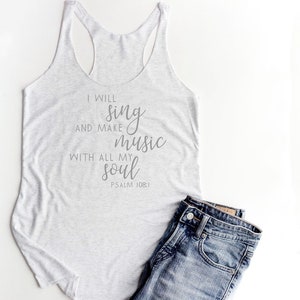 May include: A white tank top with the text "I will sing and make music with all my soul Psalm 108:1" printed on it. The tank top is paired with blue jeans.