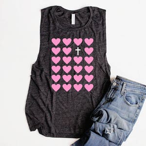 K&ouml;nnte beinhalten: Ein dunkelgraues &auml;rmelloses Tanktop mit einem Muster aus rosa Herzen und einem wei&szlig;en Kreuz in der Mitte. Das Tanktop ist aus einem weichen, bequemen Material gefertigt.