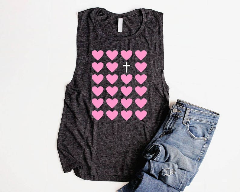 K&ouml;nnte beinhalten: Ein dunkelgraues &auml;rmelloses Tanktop mit einem Muster aus rosa Herzen und einem wei&szlig;en Kreuz in der Mitte. Das Tanktop ist aus einem weichen, bequemen Material gefertigt.