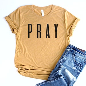 May include: A mustard yellow t-shirt with the word "PRAY" printed in black on the front.