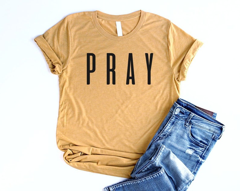 May include: A mustard yellow t-shirt with the word "PRAY" printed in black on the front.