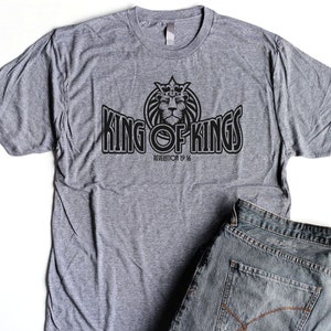 May include: A heather grey t-shirt with a black graphic of a crowned lion and the text "KING OF KINGS" with the scripture reference "REVELATION 19:16".