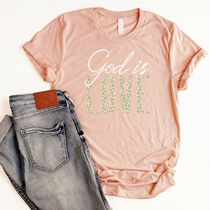 May include: A peach-colored t-shirt with the text "God is Love" in white lettering. The word "Love" is in a leopard print pattern.