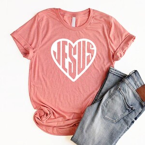 May include: A coral pink t-shirt with a white heart design that says "JESUS" inside the heart.