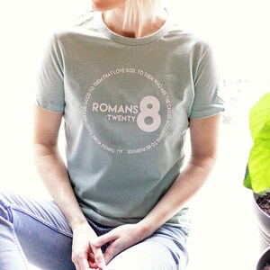 May include: A light blue t-shirt with a white circle graphic featuring the text "ROMANS :TWENTY 8" and a large white number "8" in the center.