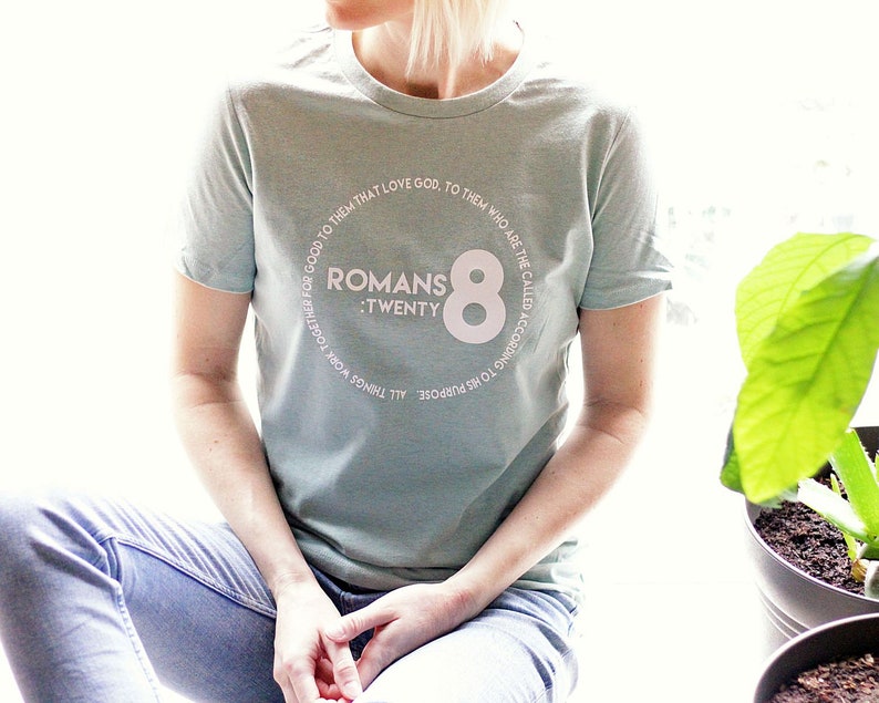 May include: A light blue t-shirt with a white circle graphic featuring the text "ROMANS :TWENTY 8" and a large white number "8" in the center.