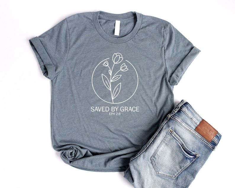 K&ouml;nnte beinhalten: Ein hellblaues T-Shirt mit einem wei&szlig;en Blumenmuster und dem Text "SAVED BY GRACE EPH 2:8".