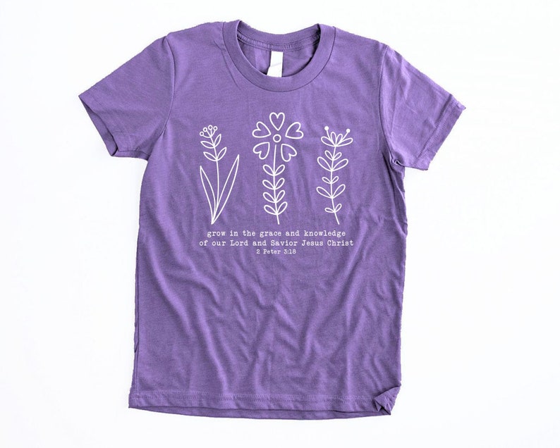 May include: Purple short-sleeved t-shirt with a white floral design and the text "grow in the grace and knowledge of our Lord and Savior Jesus Christ 2 Peter 3:10".