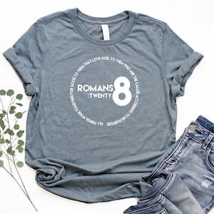 May include: A heather grey t-shirt with a white circle graphic featuring the text "Romans 8: Twenty" and the number "8" in a large font.