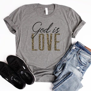 May include: A gray t-shirt with the text "God is Love" printed on it. The word "Love" is in a leopard print pattern.