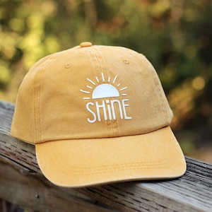 May include: A yellow baseball cap with a white sun and the word "shine" embroidered on the front.