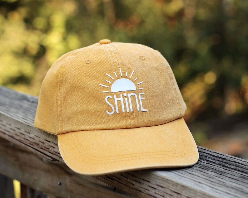 May include: A yellow baseball cap with a white sun and the word "shine" embroidered on the front.