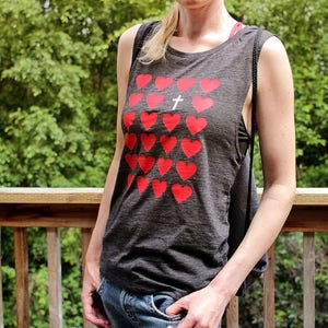 K&ouml;nnte beinhalten: Ein graues &auml;rmelloses Tanktop mit einem roten Herzmuster und einem wei&szlig;en Kreuz in der Mitte. Das Tanktop ist aus einem weichen, bequemen Material gefertigt.