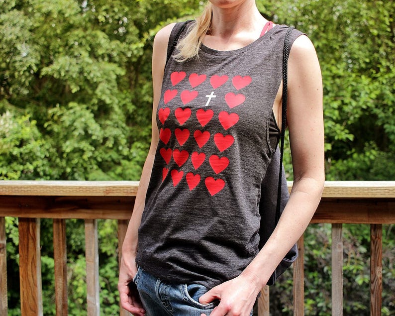 K&ouml;nnte beinhalten: Ein graues &auml;rmelloses Tanktop mit einem roten Herzmuster und einem wei&szlig;en Kreuz in der Mitte. Das Tanktop ist aus einem weichen, bequemen Material gefertigt.