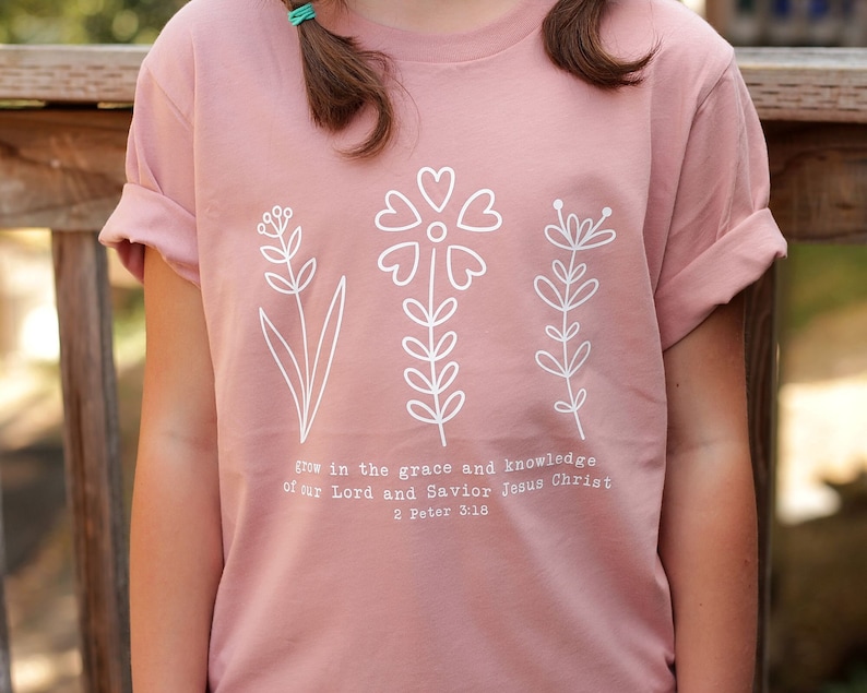 May include: A pink t-shirt with a white floral design and the text "grow in the grace and knowledge of our Lord and Savior Jesus Christ 2 Peter 3:18".