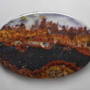 May include: Oval-shaped agate stone with a landscape design. The stone features layers of black, red, yellow, and white, resembling a natural vista. The polished surface highlights the intricate patterns and colors.